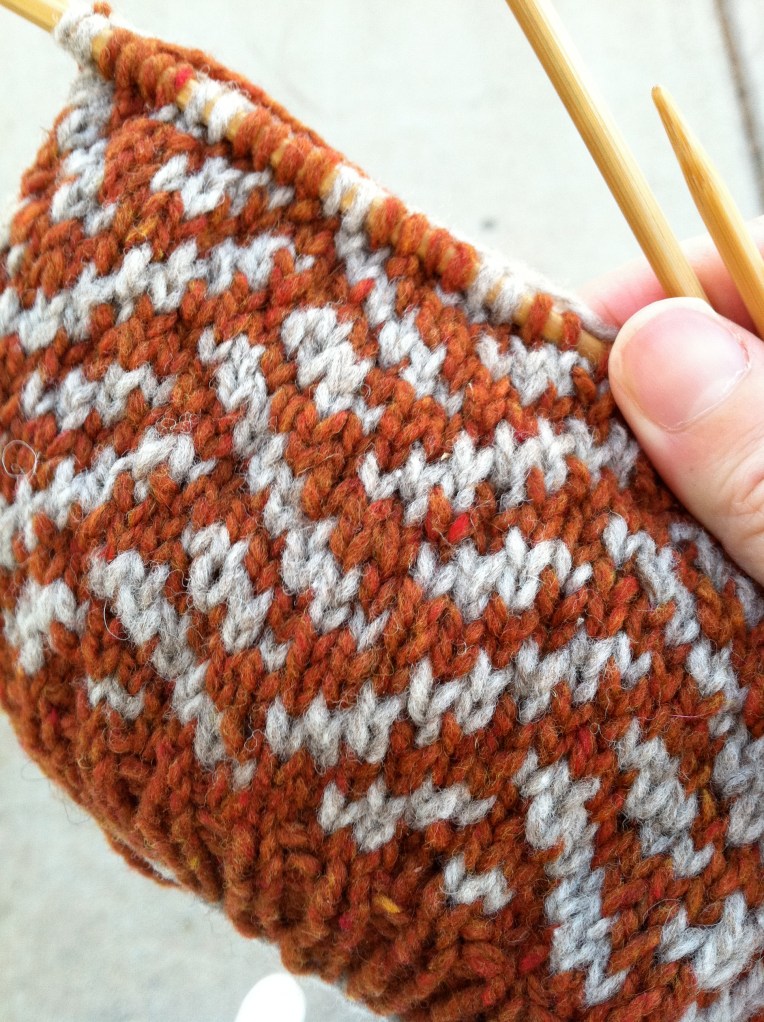 Vega Tam in Progress Orange and gray hat on knitting needles