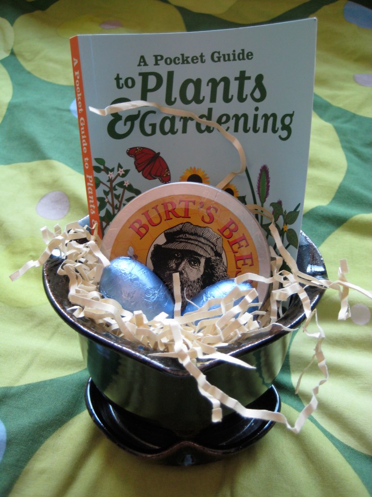 Brown stoneware flowerpot filled with small gifts and foil-wrapped chocolates.