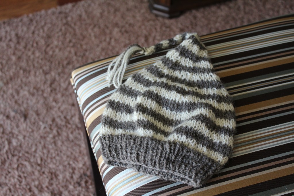 Grey and white striped knitted hat on a striped upholstered bench.
