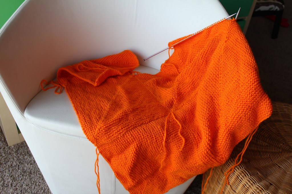 Knitted orange blanket on a white chair