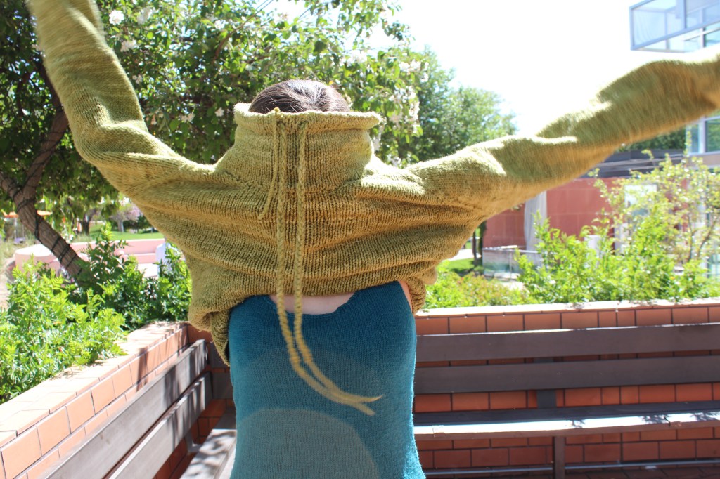 Girl putting on a green pullover sweater over a knitted tank top