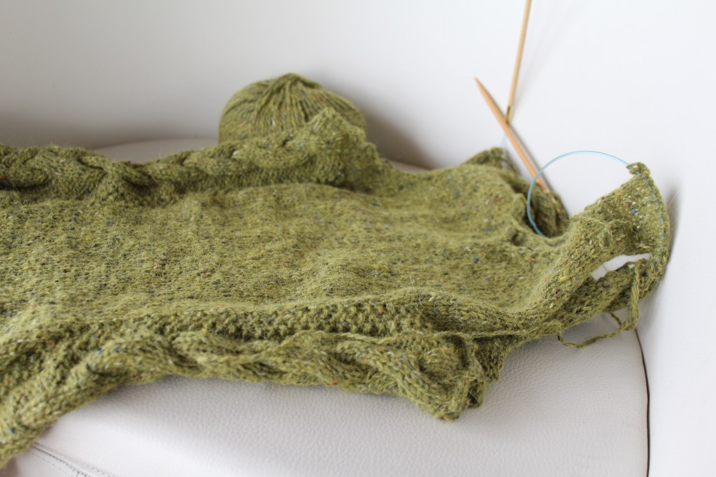 Unfinished green cabled vest on a white chair