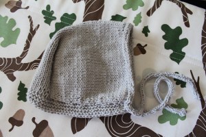 Gray baby bonnet on a brightly printed cushion