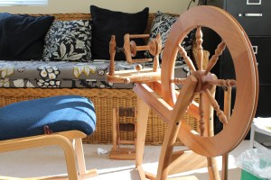 Spinning wheel, chair, and lazy Kate in front of a wicker couch
