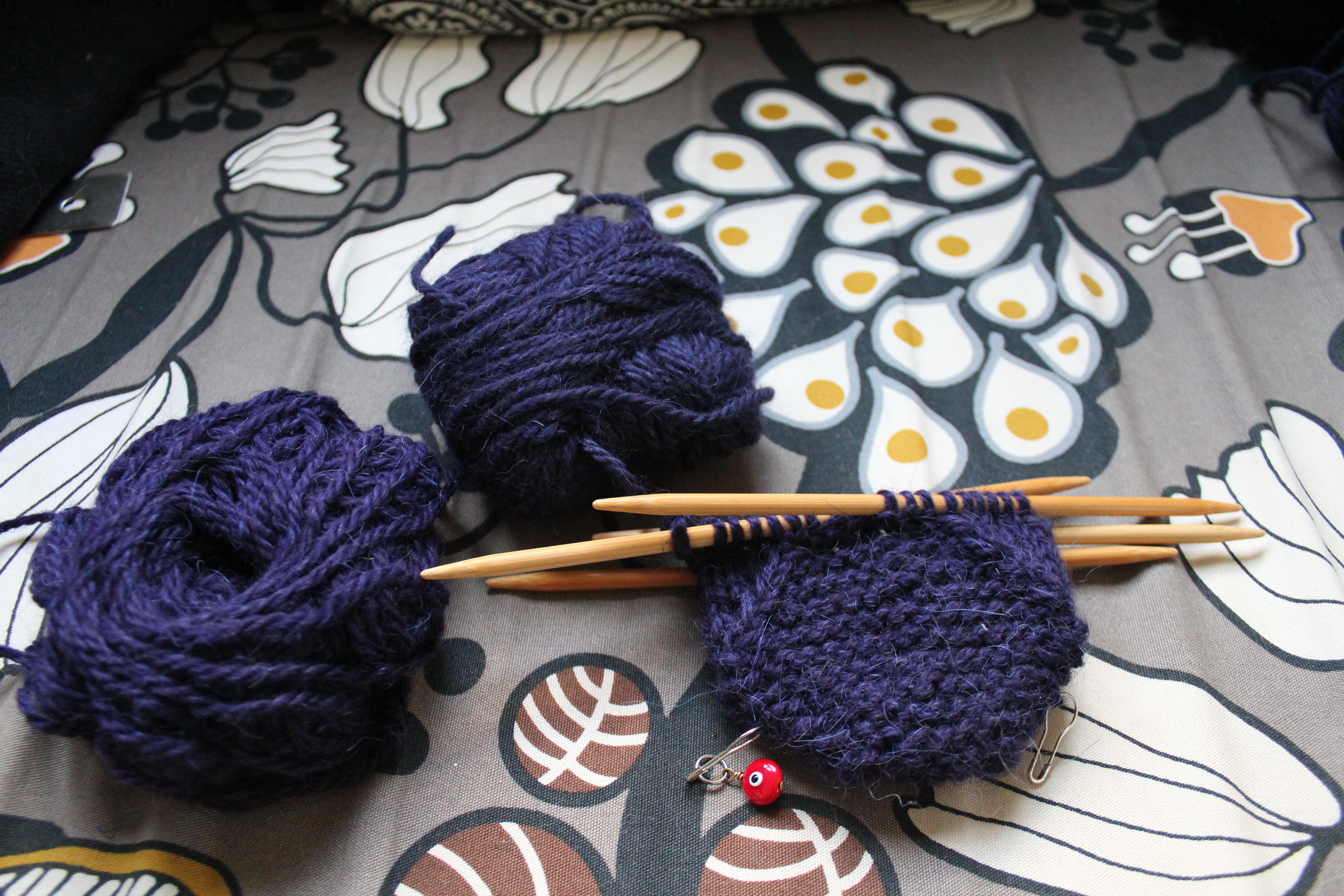 A skein of purple yarn and a skein of purplish blue yarn next to the start of a mitten