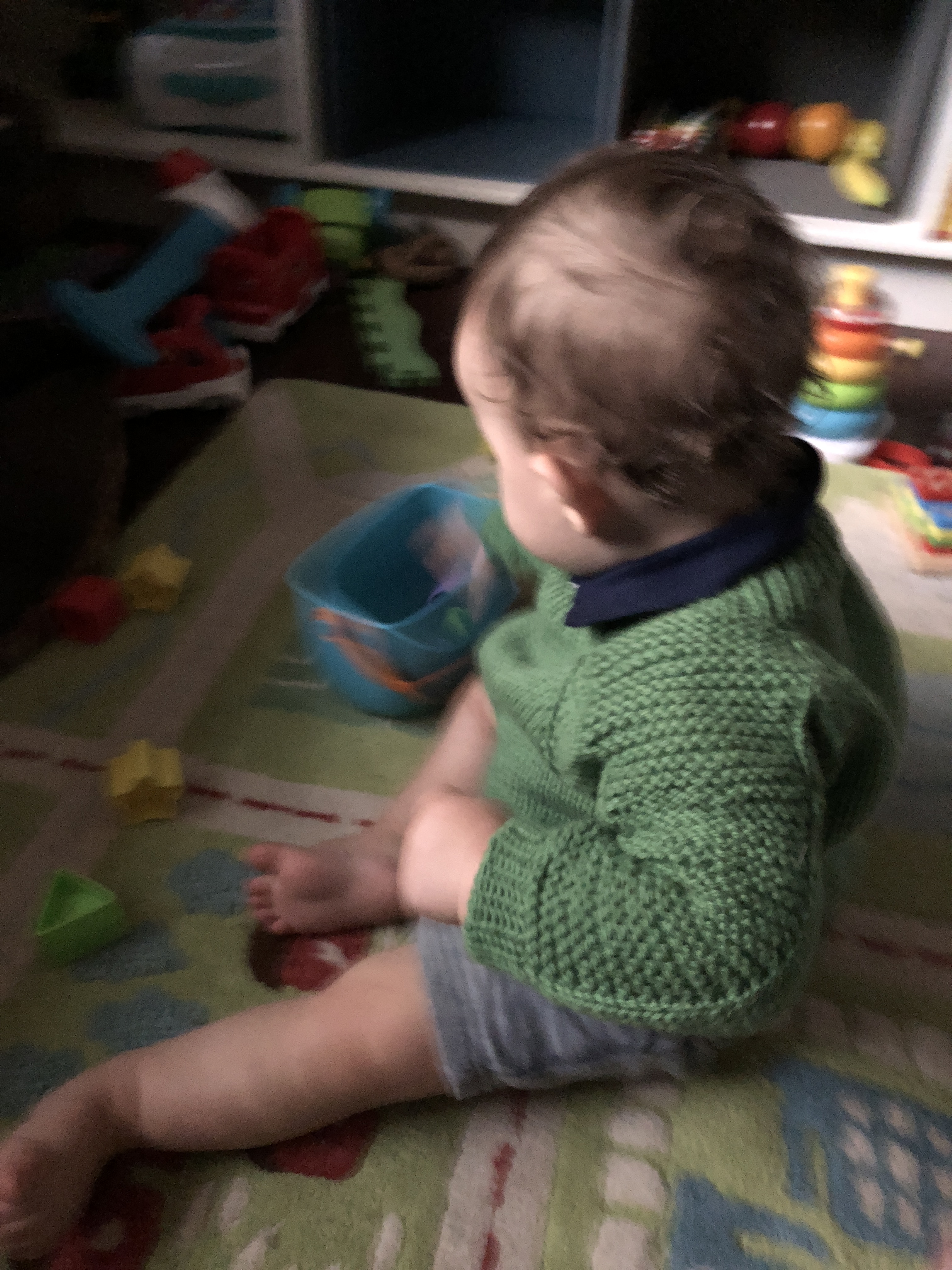 Baby playing on a colorful rug and wearing a green Flax pullover sweater