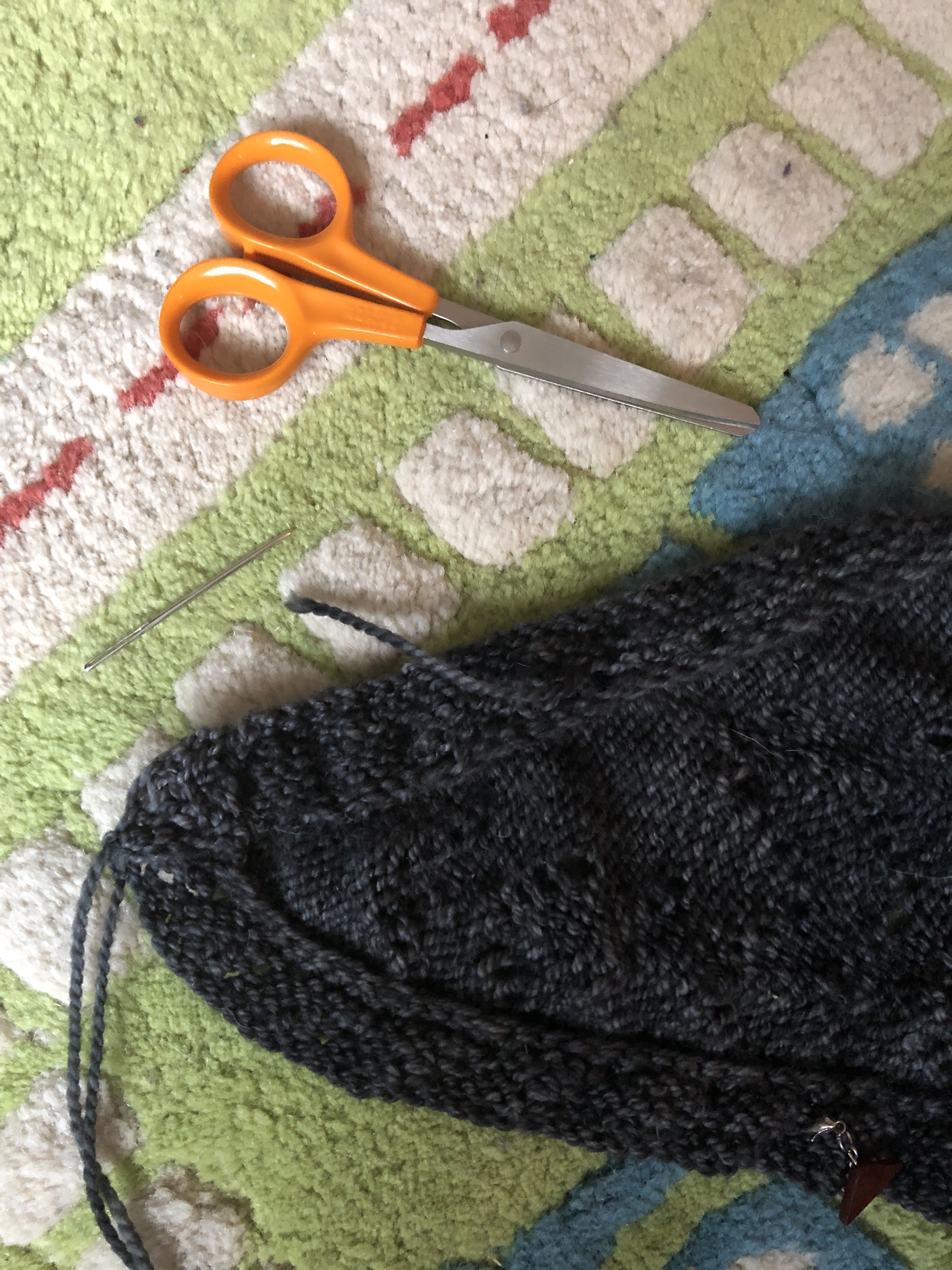 Gray Rhombuster scarf with some ends woven in on a colorful children's rug