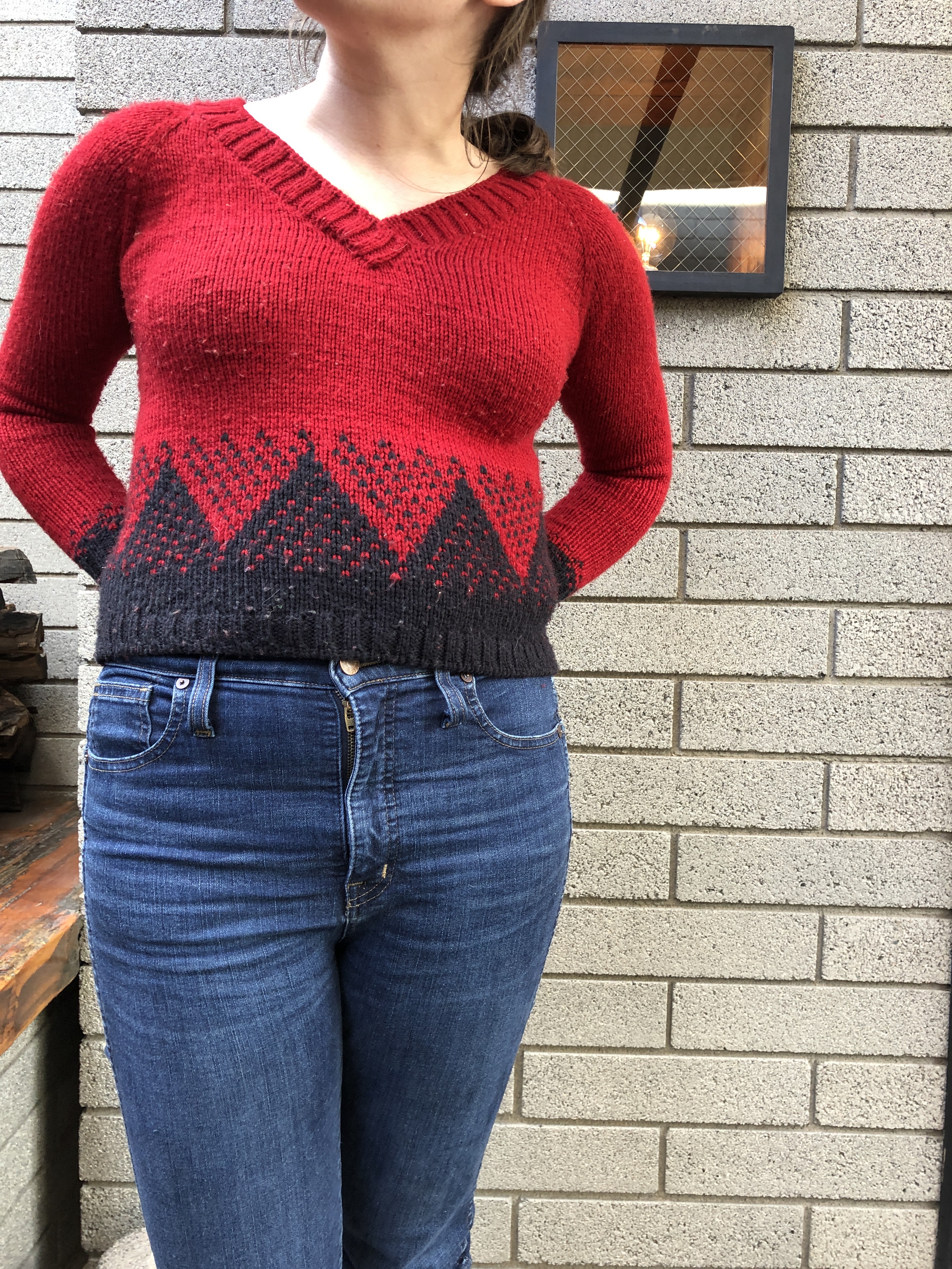 Front view of a woman wearing a red handknitted sweater with a geometric black mountain pattern