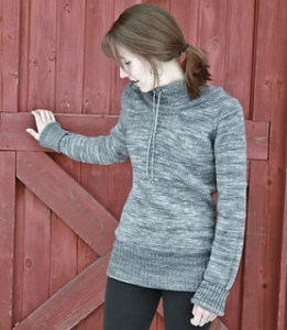 Image of a model wearing the Ease pullover by Alicia Plummer in front of a barn door, image copyright Alicia Plummer