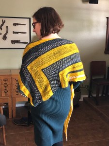 Woman seen from behind wearing a Harpers Ferry shawl in blue, golden yellow, green, and pale pink in front of vintage card catalogs