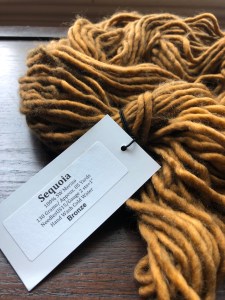 Untwisted hank of bulky Baah! Sequoia yarn in Bronze on a dark wood surface