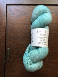 plank & stella yuki fingering in Down by the Sea, a pale turquoise, on a dark wood background