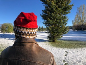 Woman wearing an Embrace My Inner Pixie hat in red with a black, gold, and white geometric brim against a backdrop of trees and light snow
