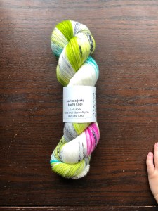 plank & stella Sock in You're a Jerky Kuchi Kopi, a pink and green speckle, on a dark wood background