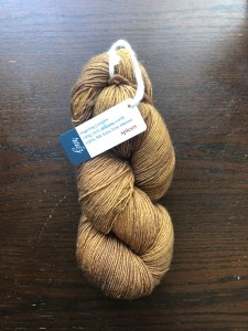 Amores Yarn Studio Raíz sock yarn in spices, a warm gold, on a dark wood background