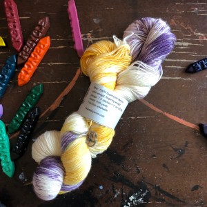 Lady Dye single-ply fingering weight in purple and yellow on a table with crayons