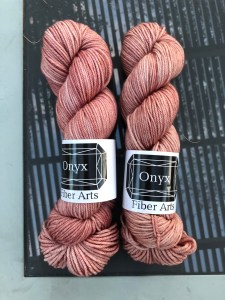 Onyx Fiber Arts Worsted in Sophia. a soft pink, on a glass table reflecting a vine-covered pergola