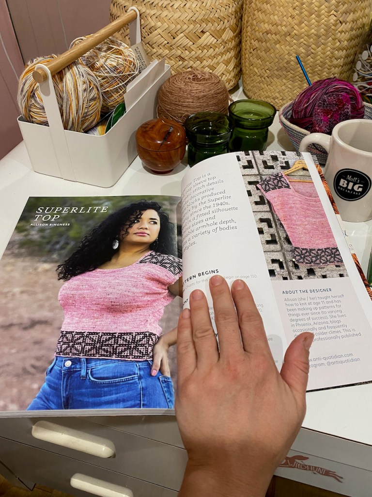 Photo of a hand atop the Superlite Top pattern page atop a cluttered desk 