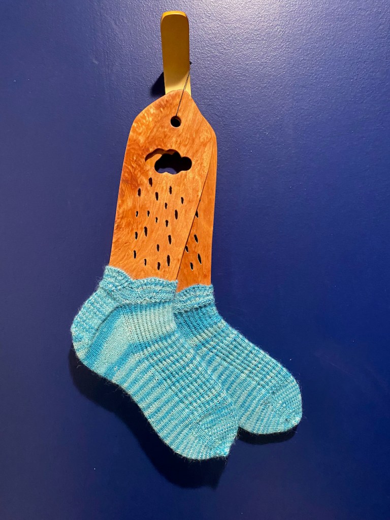 Turquoise short socks on wooden sock blockers hanging from a brass hook