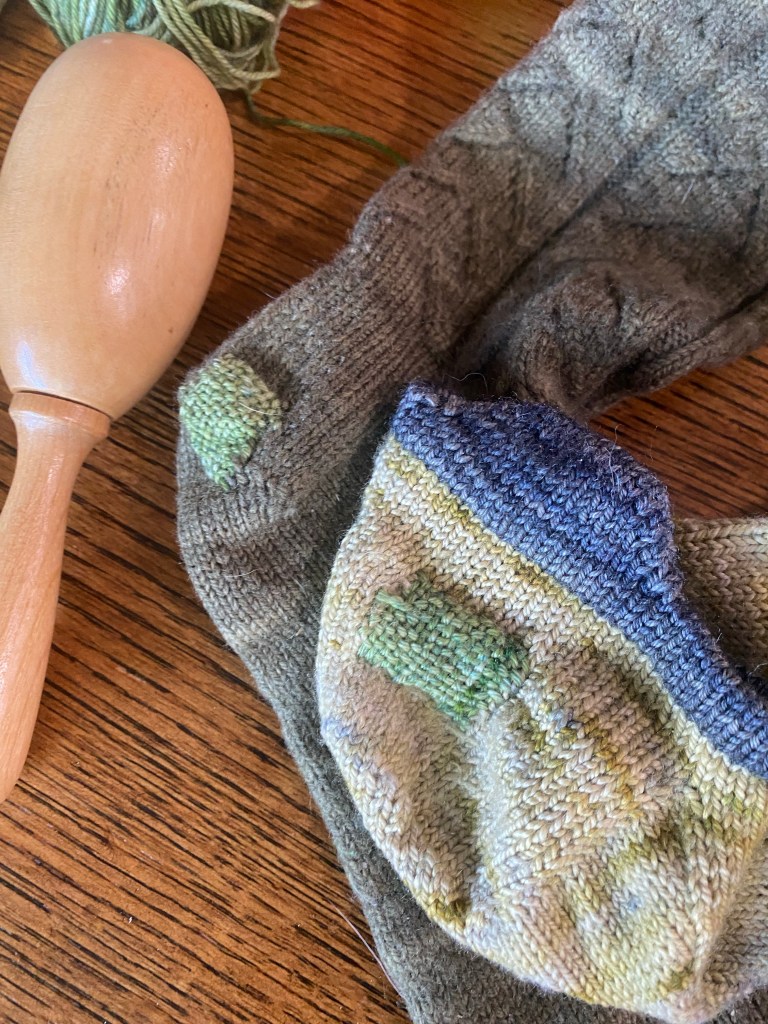 Two socks, one shirt and one crew length, in different shades of green with darning in the same shade of green