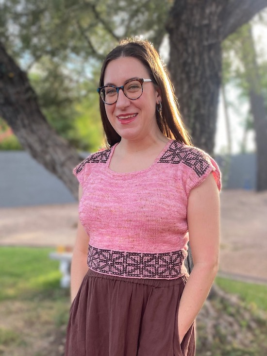 Allison, a white woman with long brown hair, modeling the Superlite Top in front of an olive tree in a garden